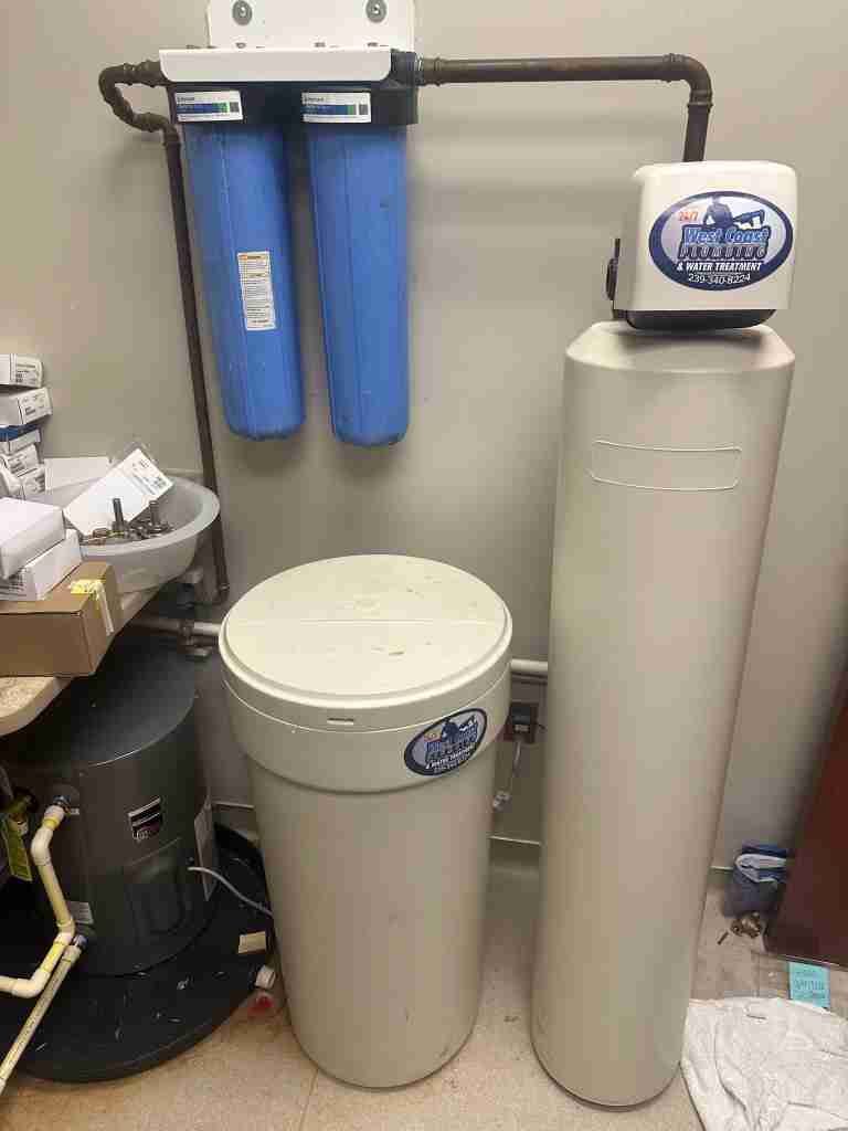 A WC Plumbing technician servicing a whole-house water treatment system beside a customer's home
