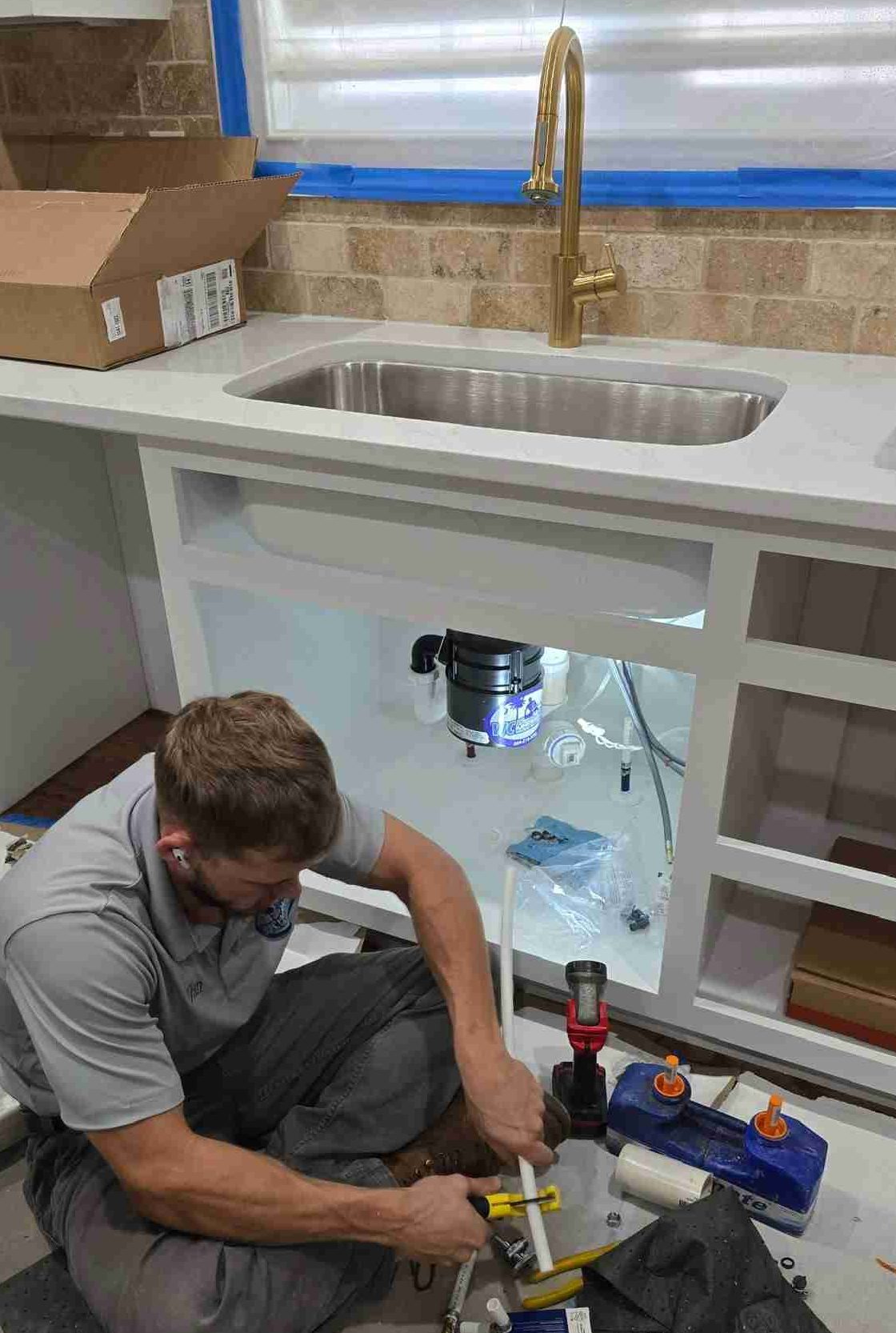 Technician repairing plumbing under a kitchen sink