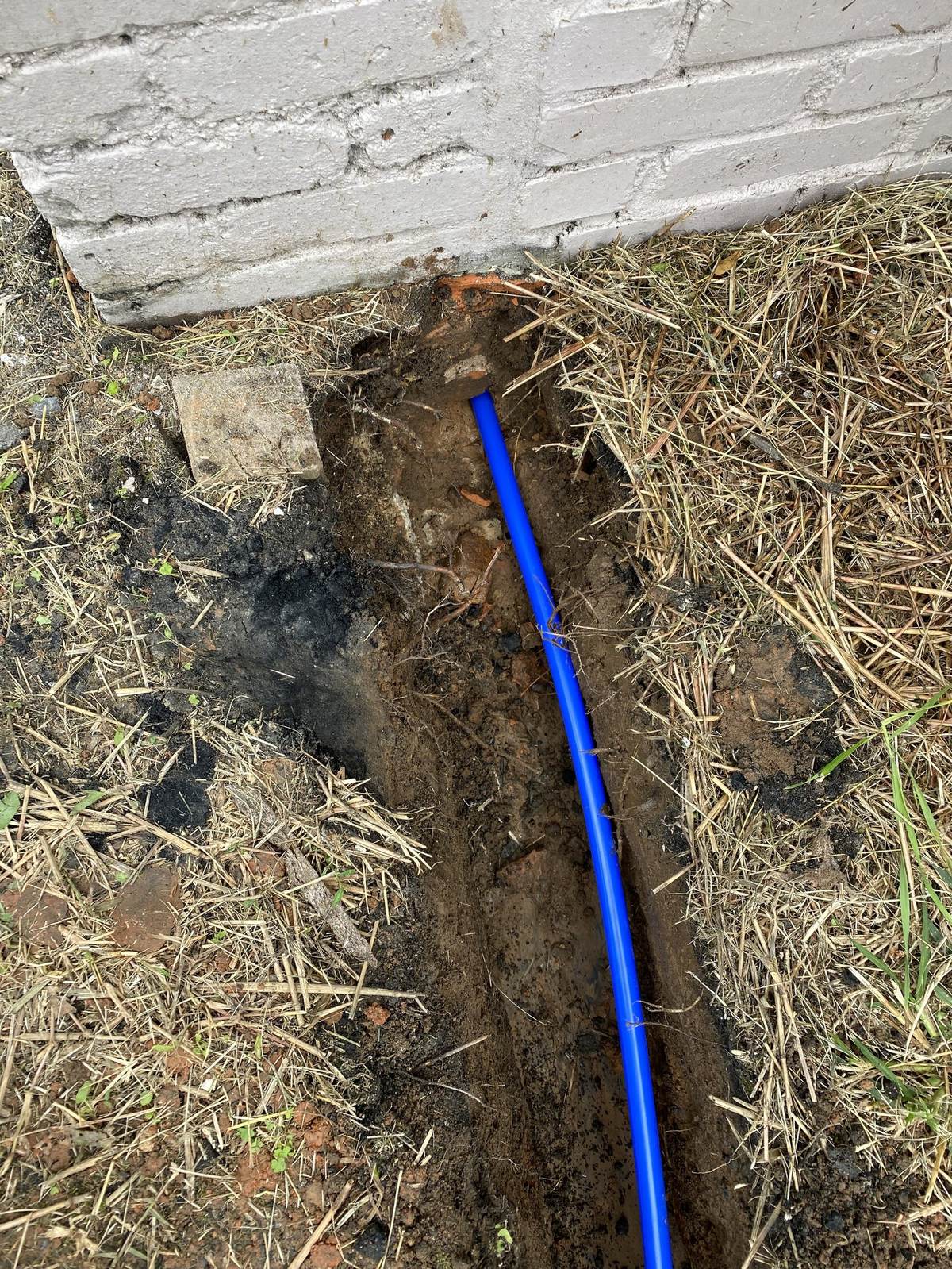 New water line laid in an open trench beside a brick foundation